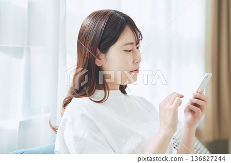 Lifestyle of a woman in her 30s operating a smartphone in the living room at home Lifestyle of a woman in her 30s operating a smartphone in the living room at home 136827244