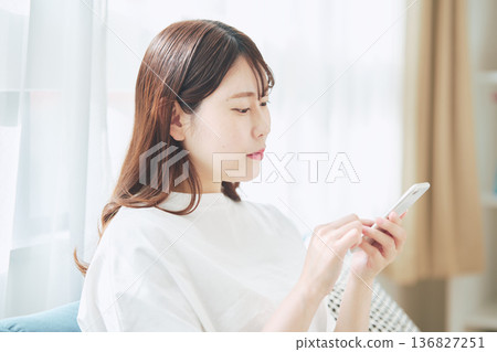 一位30多歲的女性在家中客廳使用智慧型手機的生活方式 136827251