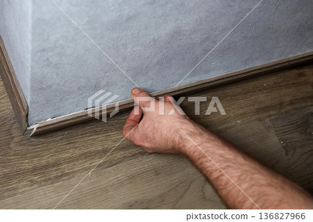 A man glues a baseboard to the base of a wall. Floor repair in a residential building 136827966