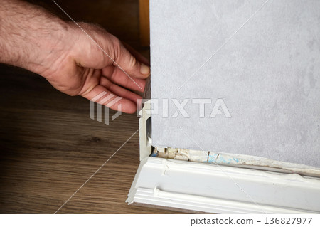 A man presses a piece of baseboard against the base of a wall with his hand. Floor repair in a residential building 136827977