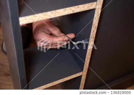 A person is putting together furniture. They hold a tool and work on securing parts. A person is putting together furniture. They hold a tool and work on securing parts. 136828000