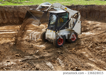 Heavy machinery moves dirt at a construction site with a clear focus on ground leveling and preparation for building Heavy machinery moves dirt at a construction site with a clear focus on ground leveling and preparation for building 136828015