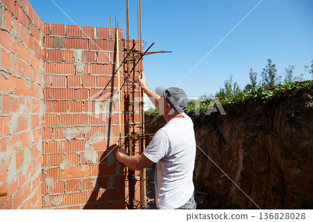 A construction worker is measuring a brick wall at a building site 136828028
