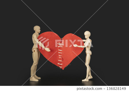 Conceptual image of two plastic mannequins holding a large red heart with stitches, symbolizing reconciliation, healing a broken heart, and saving a relationship 136828149