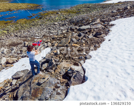 Tourist holds norwegian flag in mountains Tourist holds norwegian flag in mountains 136829150