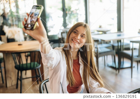 Photo of herself using smartphone. Young woman is in the cafe at daytime Photo of herself using smartphone. Young woman is in the cafe at daytime 136829191