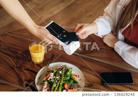 Top close up view. Woman is paying for meal by wireless payment in the cafe restaurant Top close up view. Woman is paying for meal by wireless payment in the cafe restaurant 136829248