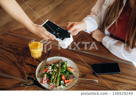 Top close up view. Woman is paying for meal by wireless payment in the cafe restaurant Top close up view. Woman is paying for meal by wireless payment in the cafe restaurant 136829249