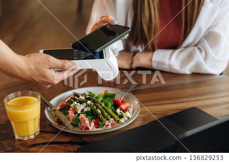 Laptop, salad and orange juice. Woman is paying for meal by wireless payment in the cafe restaurant Laptop, salad and orange juice. Woman is paying for meal by wireless payment in the cafe restaurant 136829253