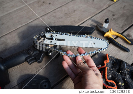 A man repairs an electric saw. Lubrication of the chain. A man repairs an electric saw. Lubrication of the chain. 136829258