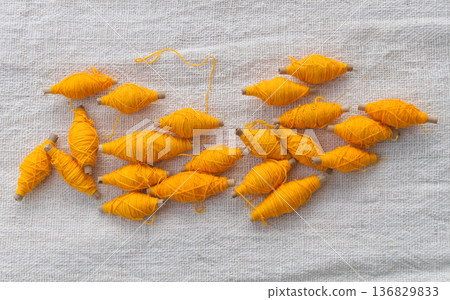 Yellow thread roll with bamboo tube placed on a white cotton background. 136829833