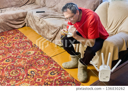 Elderly man adjusts router for wifi signal distribution in rural house. Elderly man adjusts router for wifi signal distribution in rural house. 136830262