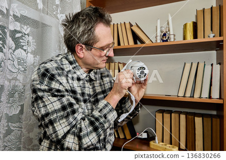 Independent installation of new surveillance camera indoors, farmer conducts tests checking settings. Independent installation of new surveillance camera indoors, farmer conducts tests checking settings. 136830266