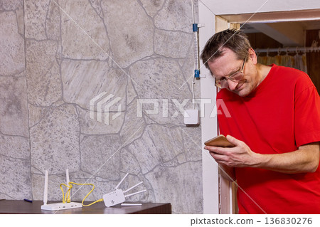Issue with setting up wifi distribution equipment elderly man uses smartphone to find solution on internet. 136830276