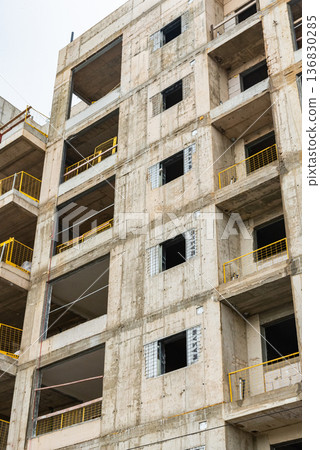 Multi-storey residential building under construction with exposed concrete framework, scaffolding and formwork in warm evening sunlight. Urban development and real estate concept. 136830285