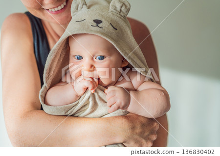 Mother holding her baby wrapped in a soft towel after bath at home, sharing a warm caring moment. Authentic parenthood scene showing love, safety and comfort. Baby hygiene, wellbeing and family 136830402
