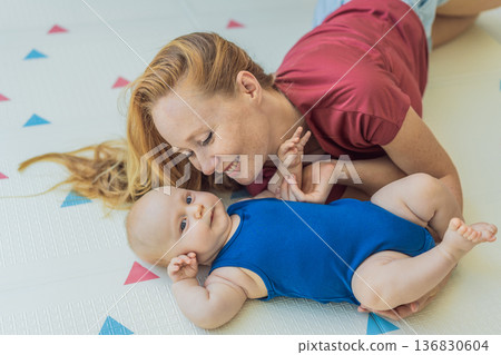 Mother and baby lying on a soft play mat at home, playing, talking and sharing a joyful moment together. Authentic family lifestyle, early childhood development and emotional bonding. Parenting and 136830604
