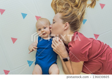 Mother and baby lying on a soft play mat at home, playing, talking and sharing a joyful moment together. Authentic family lifestyle, early childhood development and emotional bonding. Parenting and Mother and baby lying on a soft play mat at home, playing, talking and sharing a joyful moment together. Authentic family lifestyle, early childhood development and emotional bonding. Parenting and 136830605