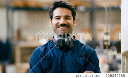 Carpenter smiling, wearing hearing protection in workshop 136830689