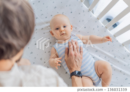 Father gently placing his baby into a crib at home, creating a calm and safe bedtime moment. Caring fatherhood scene filled with trust and warmth. Parenting, infant sleep and family bonding concept 136831339