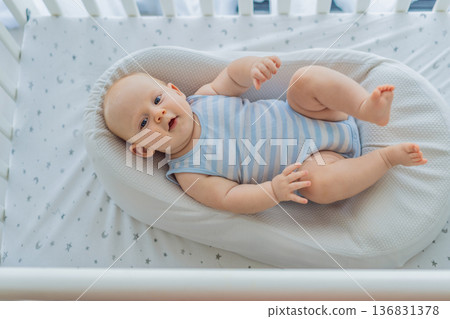 Baby lying peacefully in a cozy cocoon nest inside a crib, feeling safe and calm at home. Soft light and warm atmosphere highlight comfort and care. Infant sleep, safety and gentle parenting concept Baby lying peacefully in a cozy cocoon nest inside a crib, feeling safe and calm at home. Soft light and warm atmosphere highlight comfort and care. Infant sleep, safety and gentle parenting concept 136831378