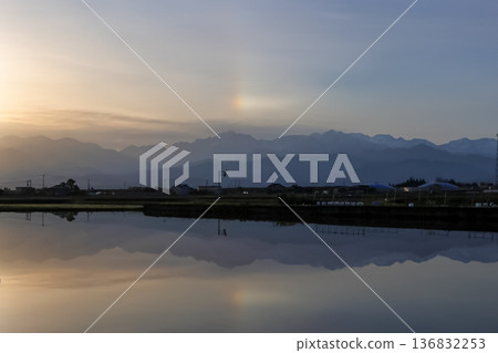 The Tateyama mountain range and the glow of the sun dog reflected in the rice paddies The Tateyama mountain range and the glow of the sun dog reflected in the rice paddies 136832253