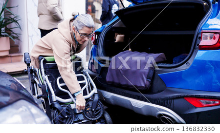 Woman folding wheelchair preparing to load into car trunk Woman folding wheelchair preparing to load into car trunk 136832330