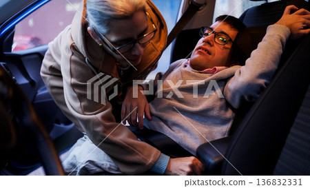 Caregiver helping man with physical impairment fasten seatbelt 136832331