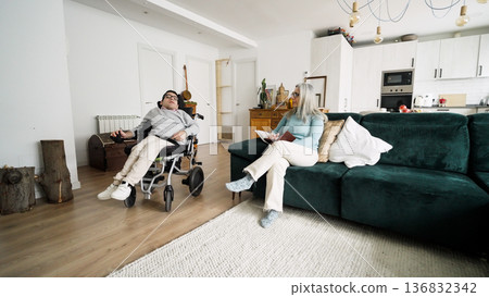 Man living with developmental condition sitting in wheelchair next to woman at home Man living with developmental condition sitting in wheelchair next to woman at home 136832342