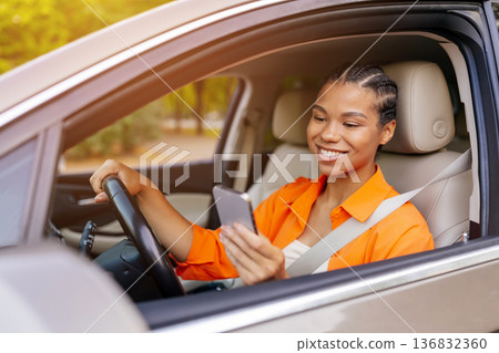 Young black woman smiling while using smartphone inside parked car 136832360