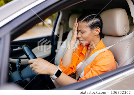 Upset black woman driving car and touching head, showing stress or headache 136832362