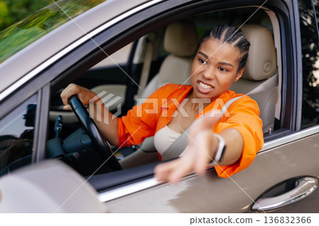 Young black woman driving car and gesturing with hand out of window Young black woman driving car and gesturing with hand out of window 136832366