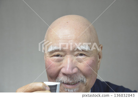 一位老人面帶微笑地喝著清酒。 136832843