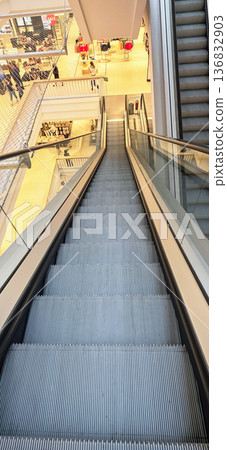Berlin, Germany - August 27, 2025: Escalator descending in modern shopping mall with bright interior design Berlin, Germany - August 27, 2025: Escalator descending in modern shopping mall with bright interior design 136832903