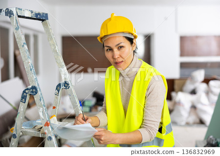 Woman worker filling documents during repair works indoors Woman worker filling documents during repair works indoors 136832969