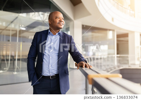 Confident mature black businessman standing in modern office atrium with bright sunlight Confident mature black businessman standing in modern office atrium with bright sunlight 136833074