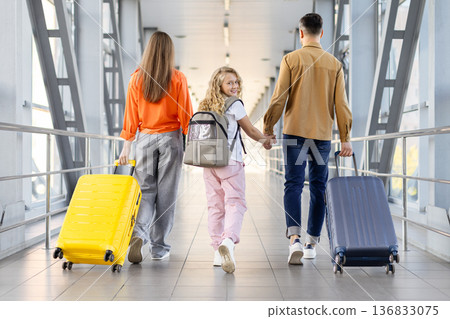 Rear view of caucasian family with suitcases walking through airport bridge 136833075