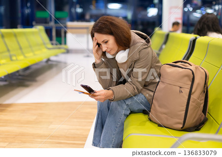 Adult caucasian woman sitting in airport terminal checking phone with worried expression Adult caucasian woman sitting in airport terminal checking phone with worried expression 136833079