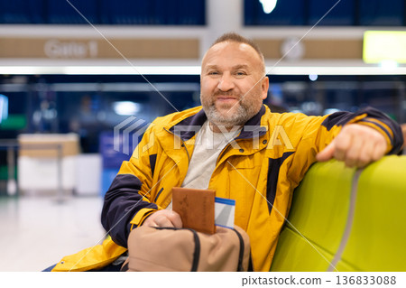 Relaxed adult caucasian man sitting in airport terminal with passport and bag Relaxed adult caucasian man sitting in airport terminal with passport and bag 136833088