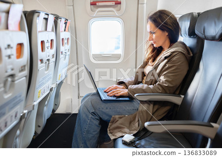 Female passenger working on laptop inside airplane cabin during flight Female passenger working on laptop inside airplane cabin during flight 136833089