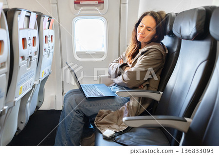 Adult woman sleeping in airplane seat with laptop on lap during flight Adult woman sleeping in airplane seat with laptop on lap during flight 136833093