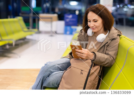 Adult caucasian woman using smartphone and passport while waiting in airport lounge Adult caucasian woman using smartphone and passport while waiting in airport lounge 136833099