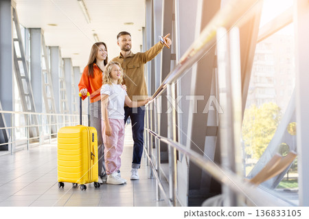 Happy family standing at airport terminal and looking through window Happy family standing at airport terminal and looking through window 136833105