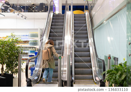 Female traveler with backpack stepping onto escalator inside airport terminal Female traveler with backpack stepping onto escalator inside airport terminal 136833110