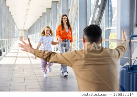 Mother and daughter walking toward father with open arms at airport Mother and daughter walking toward father with open arms at airport 136833114