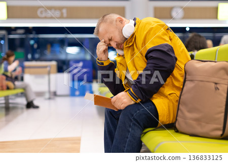 Tired adult male traveler sitting in airport lounge with passport in hand Tired adult male traveler sitting in airport lounge with passport in hand 136833125