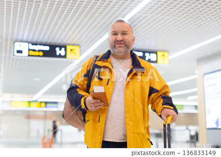 Adult caucasian male traveler walking in airport terminal with passport and luggage Adult caucasian male traveler walking in airport terminal with passport and luggage 136833149