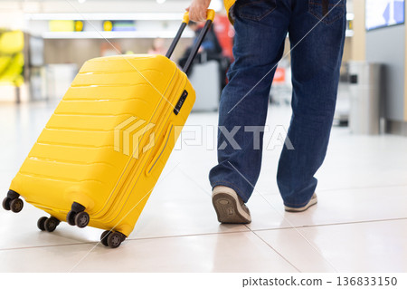 Close up of adult caucasian man pulling yellow suitcase in airport 136833150