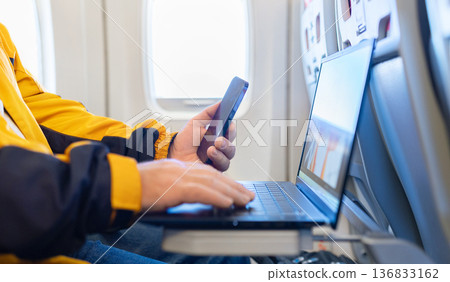 Closeup of adult man working on laptop and holding smartphone during flight 136833162