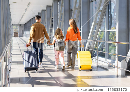 Rear view of family walking in airport terminal with suitcases and backpack Rear view of family walking in airport terminal with suitcases and backpack 136833170